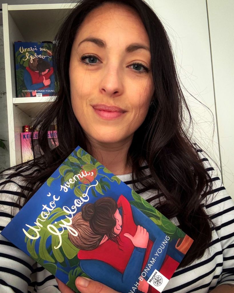 A portrait of Sanda Dominković, a smiling, dark-haired white woman, holding the book "Unatoč svemu, ljubav" in her hands.