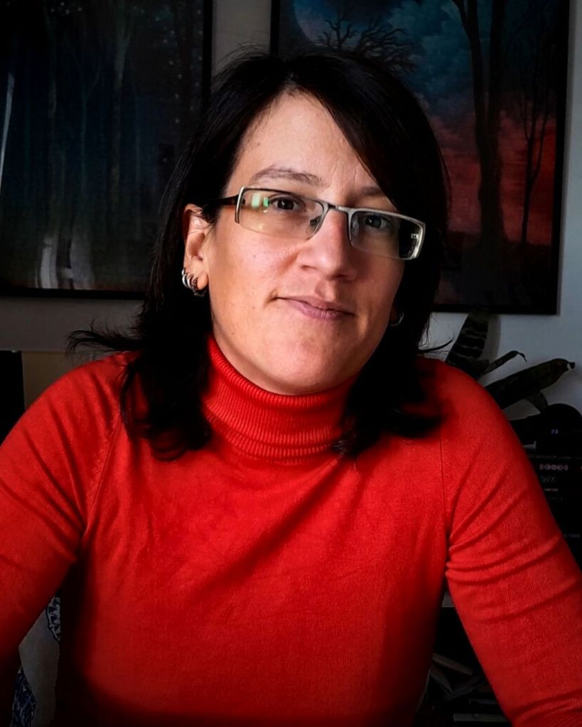 A portrait of Vesna Kurilić, a nonbinary white person with shoulder-length dark hair, with glasses.